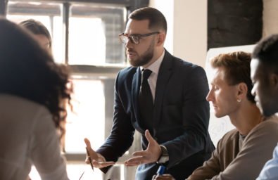 Serious businessman mentor speaking to diverse people at group training Serious businessman ceo executive mentor leader wear suit speaking to diverse business people at group meeting seminar explain corporate strategy teaching workers team at company office training